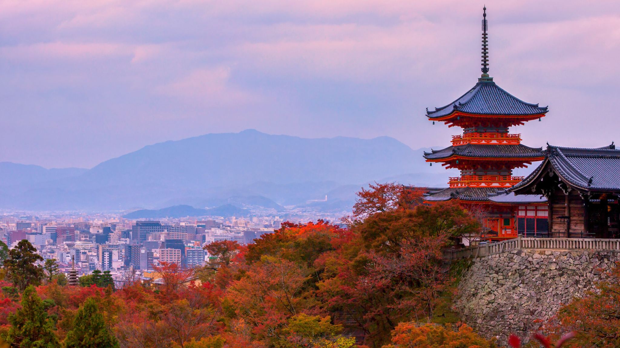 Kiyomizu-dera pagoda above autumn leaves, with Kyoto city and mountains behind